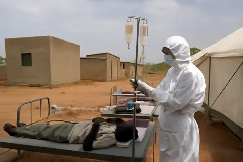Grounded editorial scene illustrating A new cholera outbreak in Sudan has resulted in more than 100 deaths, with aid efforts hindered by conflict and limited access to besieged areas such as El-Obeid.