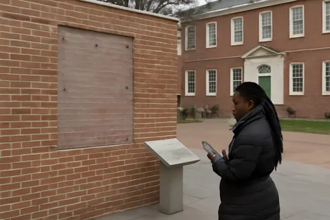 Grounded editorial scene illustrating Activists and visitors express sadness over the erasure of panels honoring enslaved Africans who served George Washington in Philadelphia’s historic President’s House.
