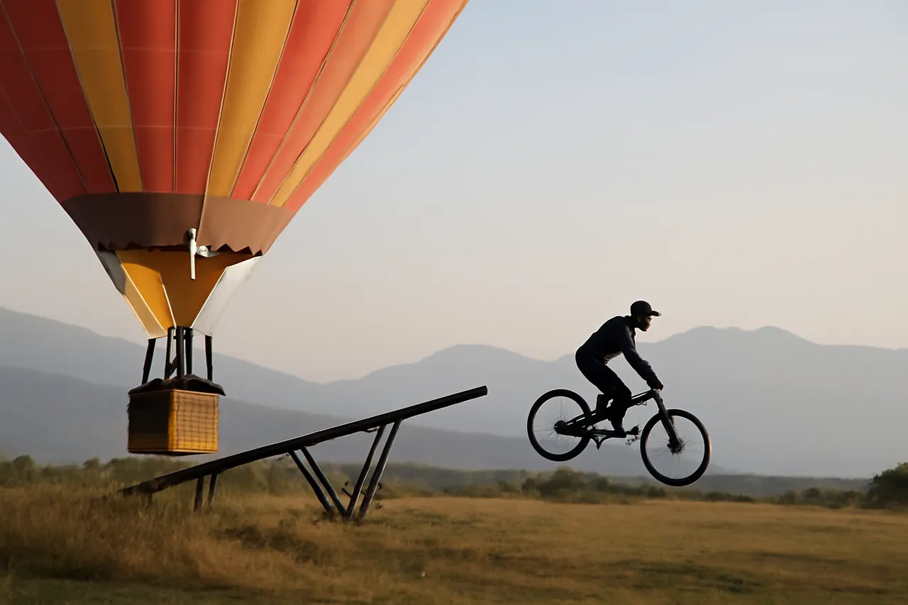 Grounded editorial scene illustrating A young Austrian mountain biker achieved a world first by riding off a hot air balloon, a stunt that took two years to prepare and was performed in Bulgaria.