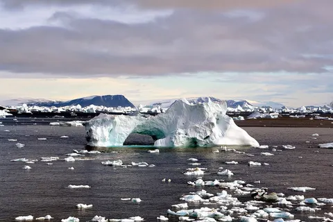 Icebergs around Cape York , Greenland . The icebergs are beautiful and display many interesting shapes. You could see the iceberg with a hole at the image. The hole was caused by weathering effects - erosion by waves, wind and melting.