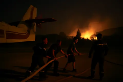 Grounded editorial scene illustrating With Canadair aircraft grounded due to low visibility, firefighters and residents work together on the ground to battle the blaze.