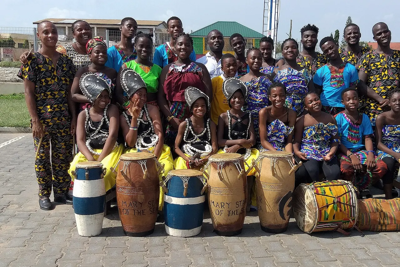 Sankorfa Traditional Dance Ensemble in a group picture with their musical instruments. Sankorfa is a word in the Twi language of Ghana that translates to "Go back and get it" and also refers to the Asante Adinkra symbol represented either with a stylized heart shape or by a bird with its head turned backwards while its feet face forward carrying a precious egg in its mouth.
