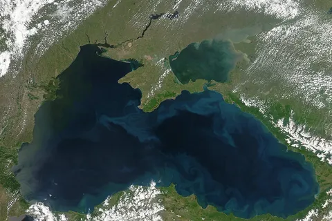 Black Sea , satellite image, May 2004. – Original image caption from Visible Earth collection of NASA: " Phytoplankton blooms and plumes of sediment form the bright blue swirls that ring the Black Sea in this Moderate Resolution Imaging Spectroradiometer (MODIS) image. Sediment flows into the sea through the vast network of rivers that empty into it. The sediment tints the water tan near the mouth of the river and green as the dirt diffuses through the water. In this image, sediment clouds the Sea of Azov in the upper right corner of the image. Two powerful rivers, the Don and the Kuban, flow into the shallow sea, depositing silt in the waters. Sediment is not the only thing that flows into the Black Sea on river water. Some of Europe’ largest rivers also deposit fertilizer from agricultural run-off in the Black Sea, and that feeds frequent phytoplankton blooms. Phytoplankton are microscopic plants that can be seen from space when large colonies grow in one place. Most of the agricultural run-off enters the Sea through the Danube River, the bright green area on the upper left side of the Sea. The water around the river’s mouths is tinted dark green, probably from the growth of surface phytoplankton. The phytoplankton blooms are a problem because their growth and decay can consume all of the available oxygen in a region, creating dead zones where fish cannot live. From the upper left corner, the countries around the Sea are Moldova , Ukraine , Russia , Georgia , Turkey , Bulgaria , and Romania . The Moderate Resolution Imaging Spectroradiometer (MODIS) on NASA’s Aqua satellite acquired this image on May 22, 2004." [data date 2004-05-22, visualization date 2004-05-25]