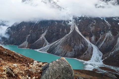 Chola glacial lake (4600) at the base of the north wall of the Cholatse-Taboche mountain massif (6440) with alluvial fans and glacial moraines under a blanket of clouds. Chola Valley, south of the Great Himalayan Range in Mahalangur Himal, Nepal, Himalayas.