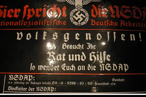 Enamel "house board" signboard for the National Socialist German Workers' Party : Haustafel der NSDAP. Hier spricht die NSDAP Nationalsozialistische Deutsche Arbeiterpartei. Decorated with Parteiadler , German national eagle of the Nazi Party. Photo taken in 2006, probably at Museum Sowjetisches Speziallager ( Speziallager Sachsenhausen , NKVD special camp Nr. 7 )