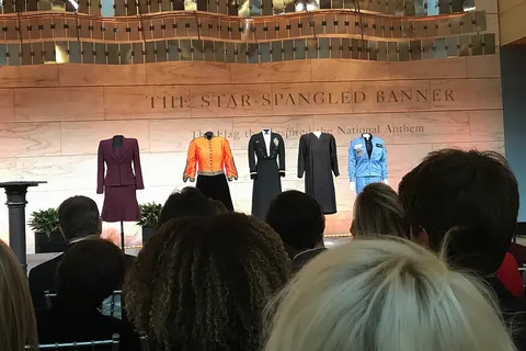 Stage at Nancy Pelosi donation ceremony at the Smithsonian's National Museum of American History. Pelosi's plum skirt suit if on the left alongside other collection items in the Smithsonian's collection including Marian Anderson's dress from her Lincoln Memorial performance, Sandra Day O'Connor's robe and Sally Ride's spacesuit.