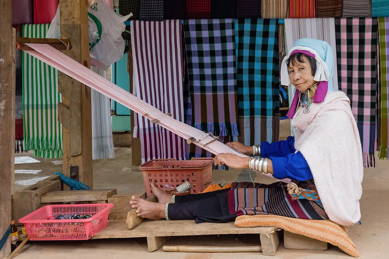 Tachileik, Myanmar: Woman of the Kayan people with decorative neck rings working at her loom.