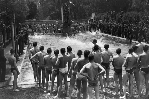 Boys in swimming togs wait at the side of an outdoor pool during swimming sports at Christ's College. Taken by an unidentified photographer, circa 1930s to 1940s.