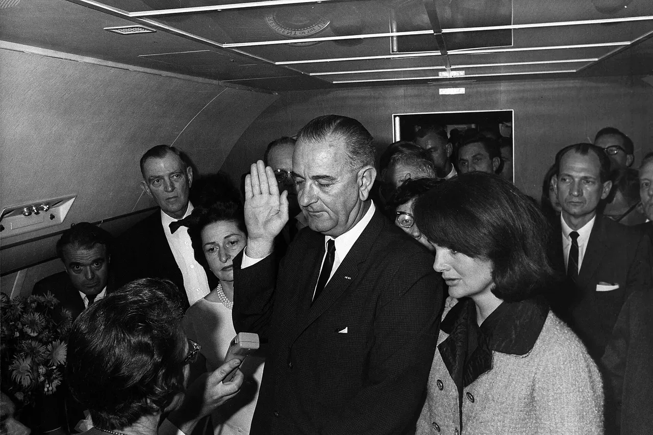 Lyndon B. Johnson taking the oath of office aboard Air Force One at Love Field Airport two hours and eight minutes after the assassination of John F. Kennedy , Dallas, Texas. Jackie Kennedy (right), still in her blood-soaked clothes, looks on. Left to right: Mac Kilduff (holding dictating machine), Judge Sarah T. Hughes , Jack Valenti , Congressman Albert Thomas , Marie Fehmer (behind Thomas), First Lady Lady Bird Johnson , Dallas Police Chief Jesse Curry , President Lyndon B. Johnson , Evelyn Lincoln (eyeglasses only visible above LBJ's shoulder), Congressman Homer Thornberry (in shadow, partially obscured by LBJ), Roy Kellerman (partially obscured by Thornberry), Lem Johns (partially obscured by Mrs. Kennedy), former First Lady Jacqueline Kennedy , Pamela Turnure (behind Brooks), Congressman Jack Brooks , Bill Moyers (mostly obscured by Brooks), White House correspondent Sid Davis (behind Brooks, looking down)