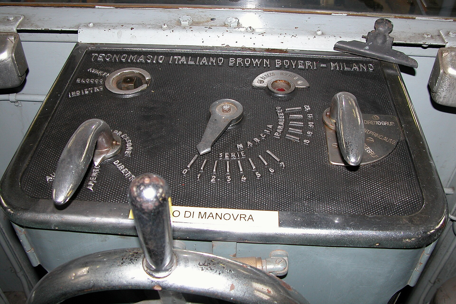 La placca del banco di manovra della cabina anteriore della locomotiva elettrica FTC 13. A sinistra della lancetta indicatrice si può notare l'abrasione delle sette tacche corrispondenti alla frenatura elettrica, marcate inizialmente con la scritta FRENO e i numeri da 1 a 7. Lo spazio occupato dalla spia BLOCCO INSERITO era dedicato in origine al comando dell'indebolimento di campo dei motori di trazione; infatti alla sua sinistra si possono notare, seppur con difficoltà, i segni dell'abrasione delle scritte originali AVVIAMENTO e ACCELERAZ. Per le scritte originali della placca cf Massimo Condolo, Torino – Ceres. 140 anni di storia dalla "Ciriè-Lanzo" alla metropolitana regionale , Brescia, Fondazione Negri, 2008, foto p. 76.
