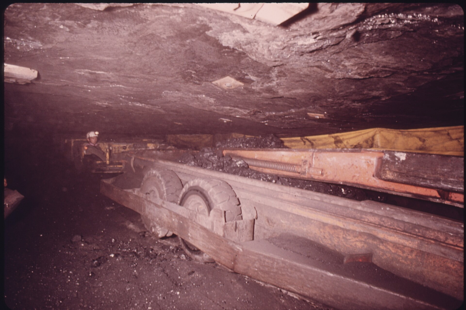 SHUTTLE CAR OF COAL IN A THREE FOOT SHAFT IN A MINE OWNED BY THE TENNESSEE CONSOLIDATED COAL COMPANY NEAR JASPER AND CHATTANOOGA, TENNESSEE. THE SHUTTLE IS PUSHED BY A TRACTOR AND HAS A HYDRAULIC PUSH WHICH SHOVES THE COAL ONTO A CONVEYOR BELT WHICH TAKES THE MATERIAL OUT OF THE MINE. IT IS CALLED A NON-GASSY MINE BECAUSE IT IS ABOVE THE SURROUNDING WATER TABLE. THE YELLOW CANVAS BARELY VISIBLE OVER THE TOP OF THE SHUTTLE IS USED TO DIRECT FRESH AIR INTO THE MINE