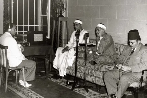 King Farouk I of Egypt listening to the Dhikr al-Hakim Quranic verses, which were broadcast during Ramadan from Abdeen Palace in the presence of Sheikh Taha al-Fashni (seen here reciting in the microphone) and Sheikh Mustafa Ismail .