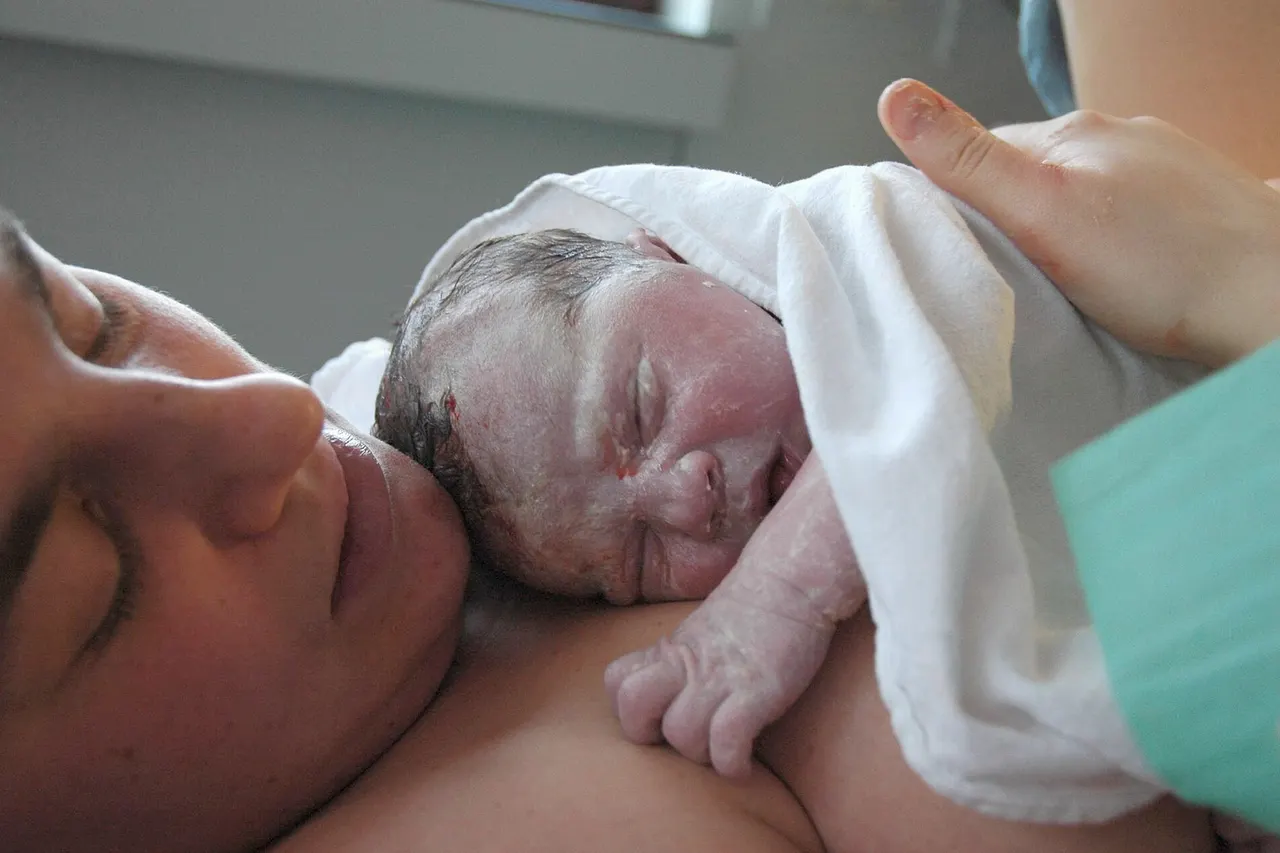 Baby on mother's belly right after birth, skin covered in vernix and some blood.