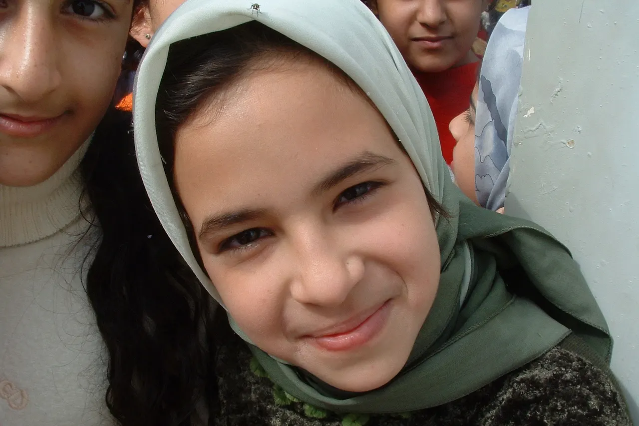 Iraqi girl smiles . Iraqi girl living next to Al Daura Oil Refinery in Baghdad pauses for a smile amongst jostling children. I managed to snap a picture of this stunning looking Iraqi girl while I was touring Al Daura Oil Refinery as part of the Human Shield Action to Iraq . I took this photo, and many more, of the children living next to the refinery where their parents worked. They were all quite enjoying themselves and I managed to get mobbed a couple of times. I often look back on this photo and wonder if she, and her friends, are still alive. I hope to go back one day and find out. — Christiaan 11:58, 5 Feb 2005 (UTC)